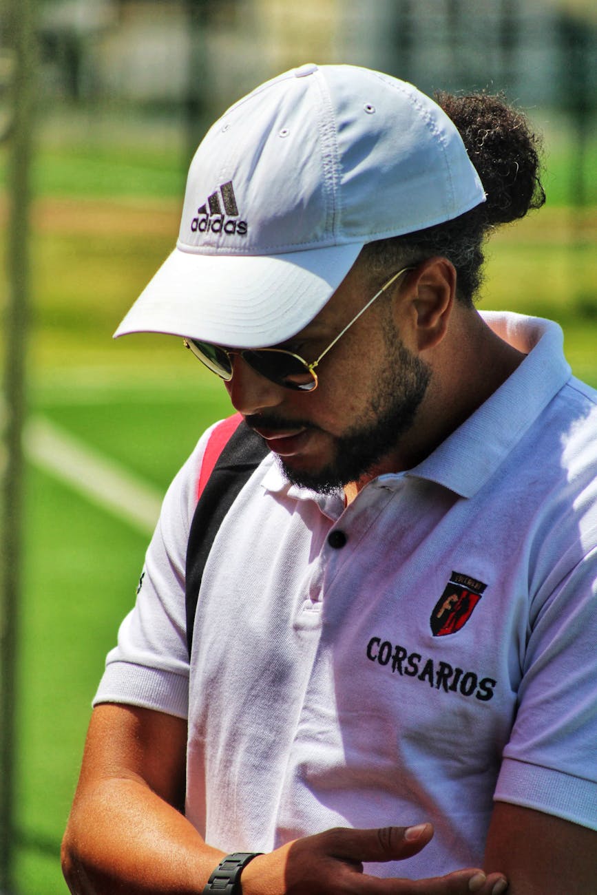 male coach on field wearing white cap and sunglasses
