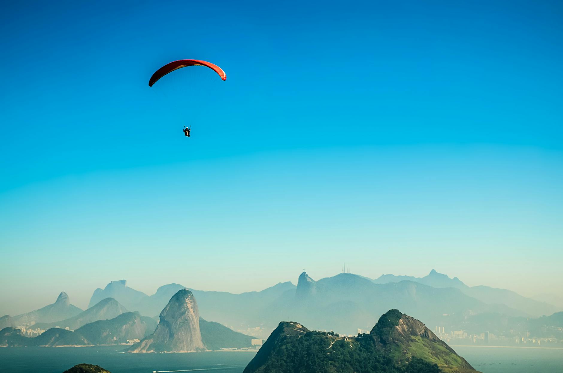 panorama photo of a person parachuting above volcano lake during daytime