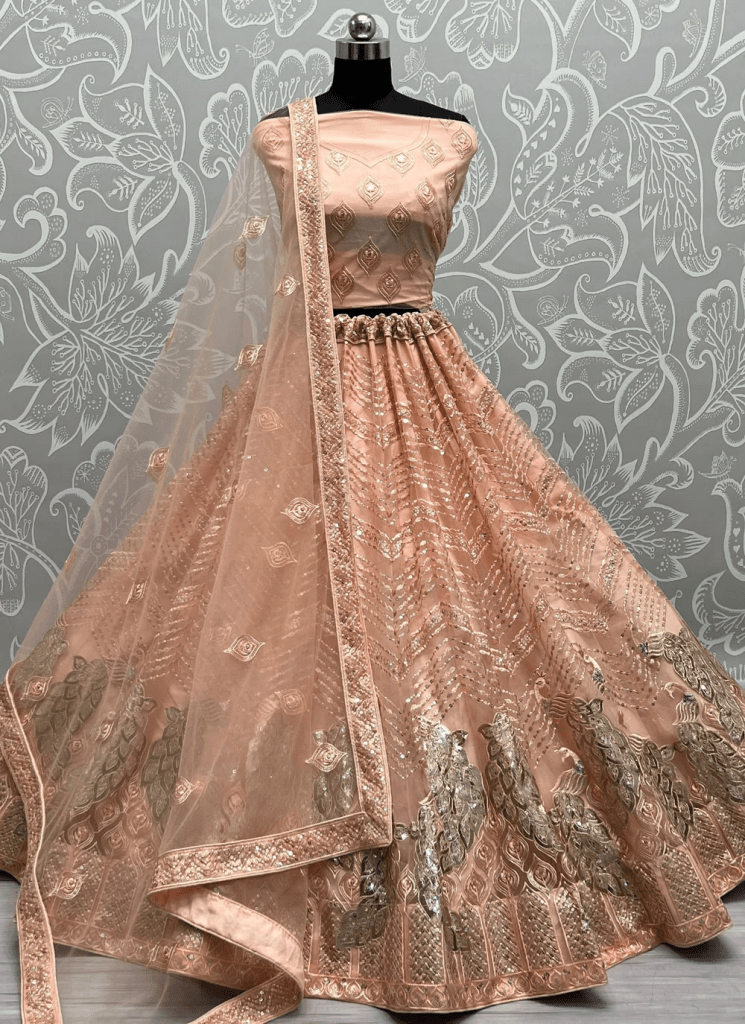 A pastel bridal lehenga in blush pink, featuring intricate embroidery and a matching dupatta, displayed on a mannequin against a floral background.